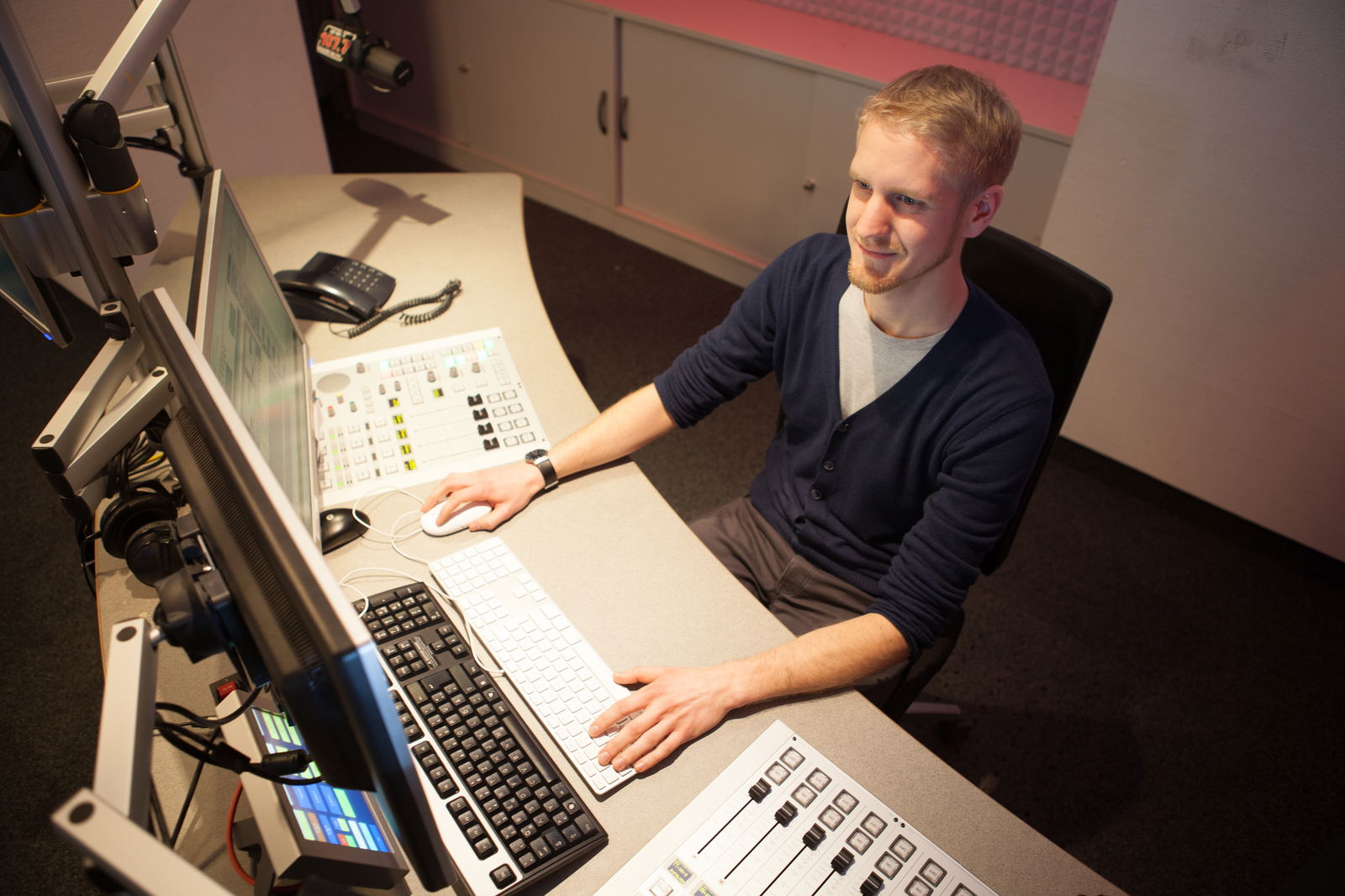 Ein junger Mann sitzt an einem Rechner mit Mischpult in einem Radiostudio.