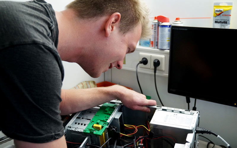 Ein Kollege aus der technischen Abteilung begutachtet einen Rechner an seiner Werkbank