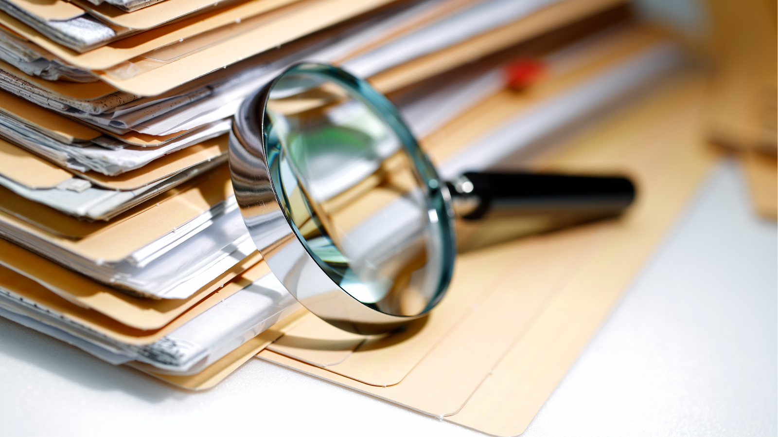 Akten die auf einem Tisch liegen davor liegt ein Lupe.