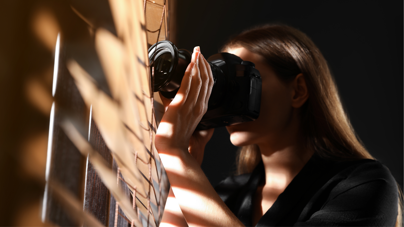 Eine Frau spioniert mit einer Digitalkamera durch den Vorhang.